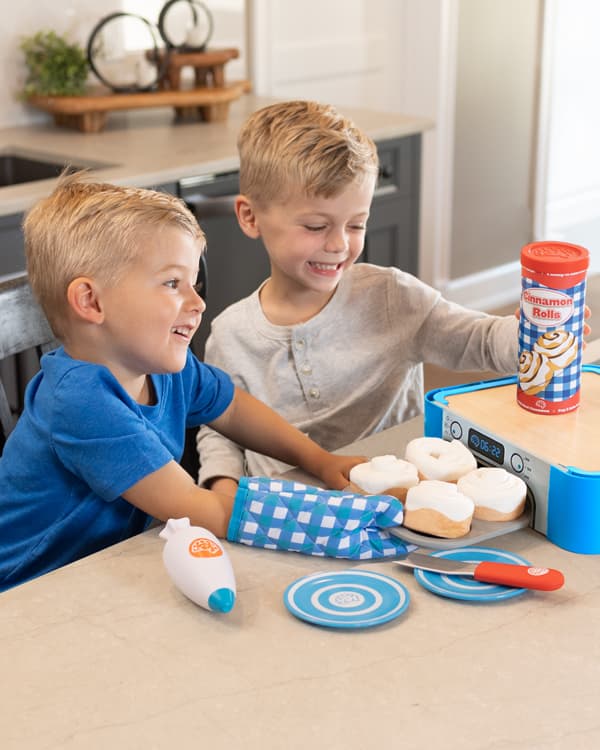 Child in a kitchen smiling and playing with Pretendables Cinnamon Roll Set